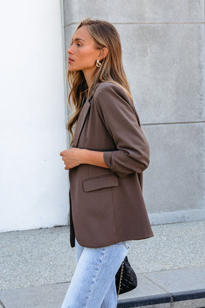 Woman in the Day To Night Blazer - Mocha and light blue jeans stands outdoors, holding a black quilted bag.