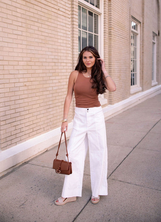 Woman on a sidewalk in a brown sleeveless top, Deluxe Ivory Wide Leg Denim Pants, sandals, and holding a brown handbag.