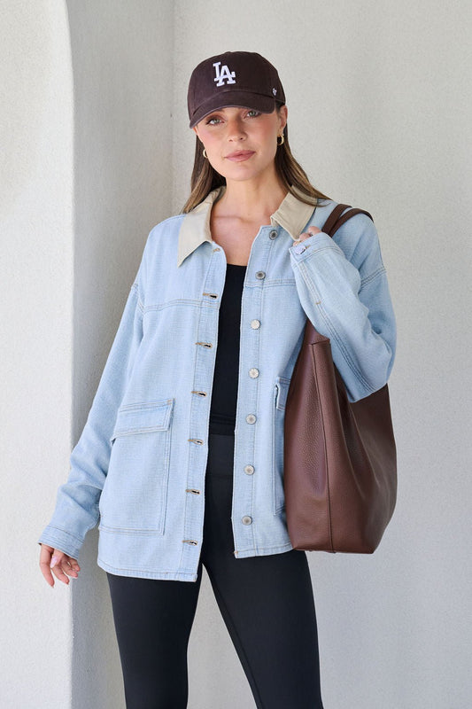 Woman in a black LA cap, Denim Buttoned Utility Jacket, black top, leggings, and a large brown tote bag.