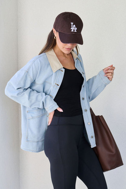 A woman in a Denim Buttoned Utility Jacket, black LA cap, black top, and leggings holds a brown tote bag while looking down.