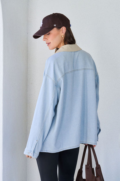 Woman wearing a Denim Buttoned Utility Jacket, black leggings, brown cap, and holding a brown bag, facing away.