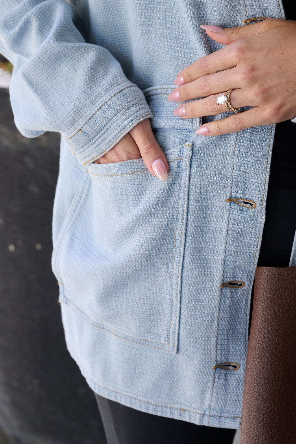 A person with manicured nails and rings slips their hand into the pocket of a Denim Buttoned Utility Jacket.