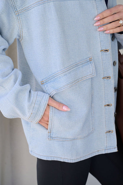 A person wears the Denim Buttoned Utility Jacket, one hand in the pocket, showing manicured nails and a gold ring.