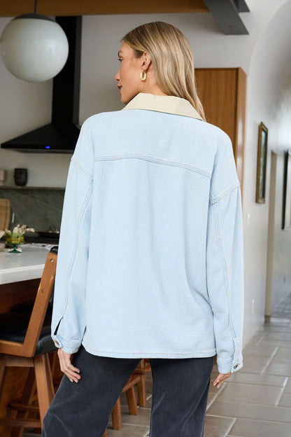 A woman with long blonde hair wears a Denim Buttoned Utility Jacket indoors, back turned to the camera.