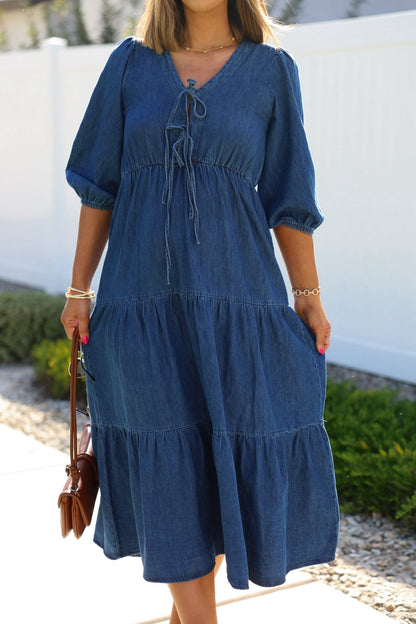 Woman wearing the Denim Front Tie Tiered Midi Dress - FINAL SALE, standing outdoors holding a brown handbag.