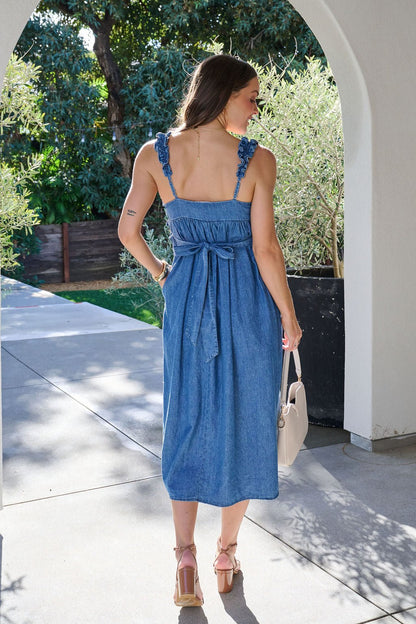 Woman in a Denim Ruffle Smocked Midi Dress, featuring a bow waist, stands outdoors with her back to the camera.