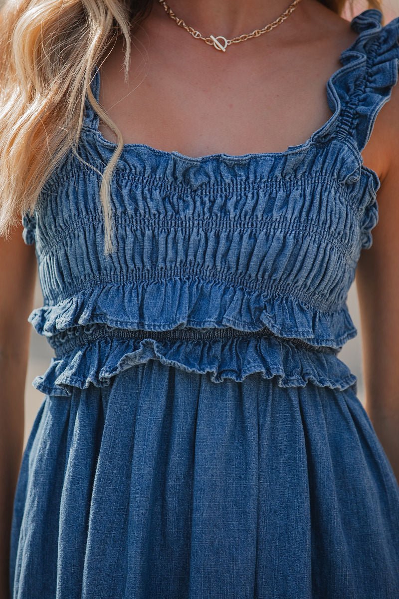 Woman in a blue Denim Ruffle Smocked Midi Dress and gold chain necklace, shown from shoulders to waist.