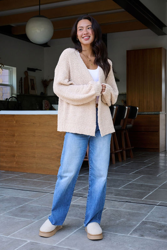 Woman wearing the Desert Rose Popcorn Textured Open Front Cardigan, white top, blue jeans, and beige slippers, smiling indoors.
