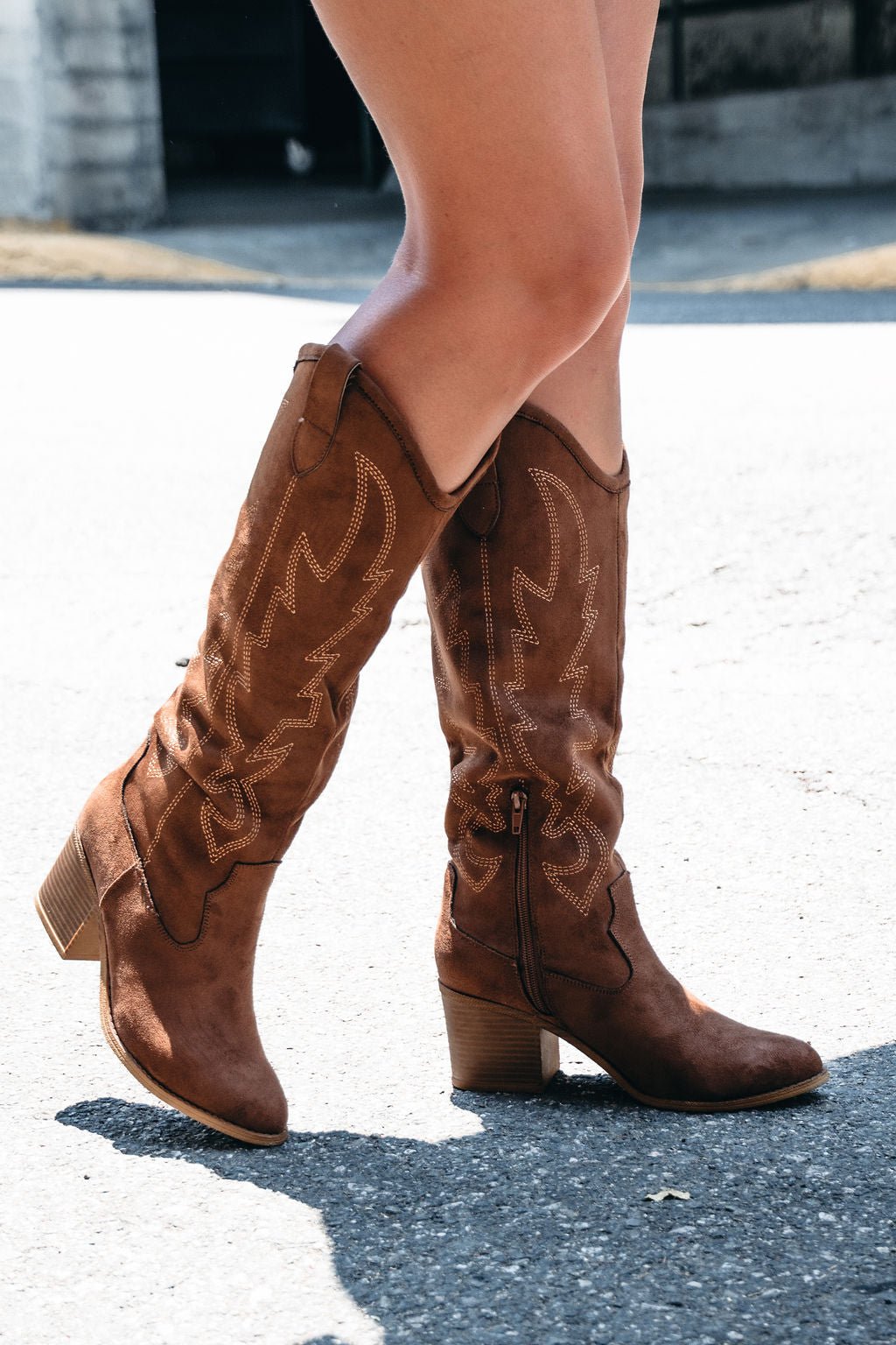 Person wearing Dirty Laundry Upwind Suede Western Boots in brown, walking outdoors on a sunny day.
