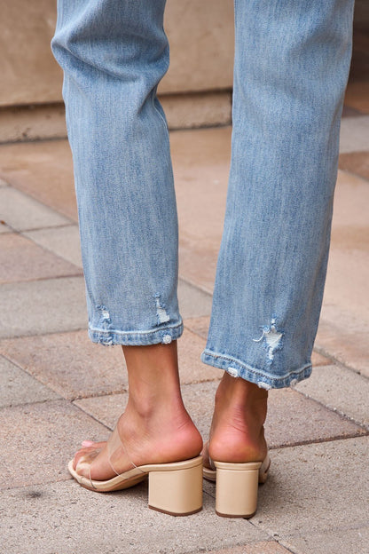 Someone wears Distressed Slim Straight Leg Jeans - Medium Wash and beige heeled sandals while standing on stone pavement.