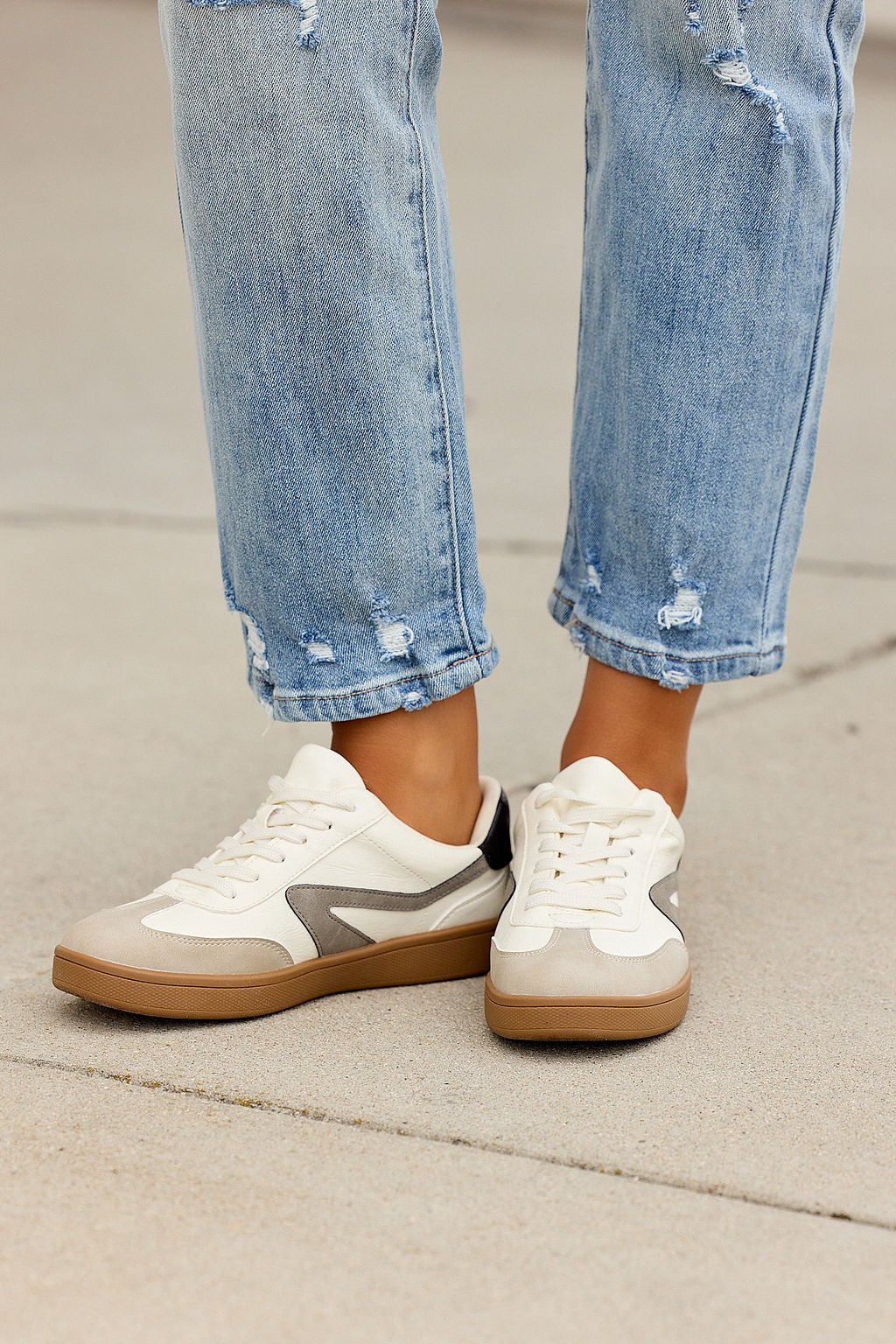 Person in light-wash ripped jeans and Dolce Vita Voyage Sneakers - Grey, standing on concrete.