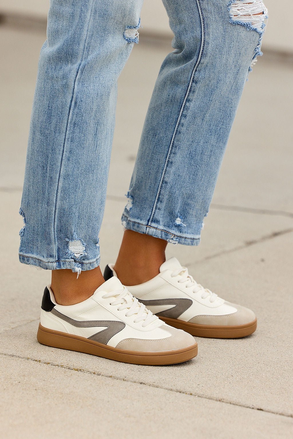 Someone in light blue ripped jeans and Dolce Vita Voyage Sneakers - Grey stands on a concrete surface.