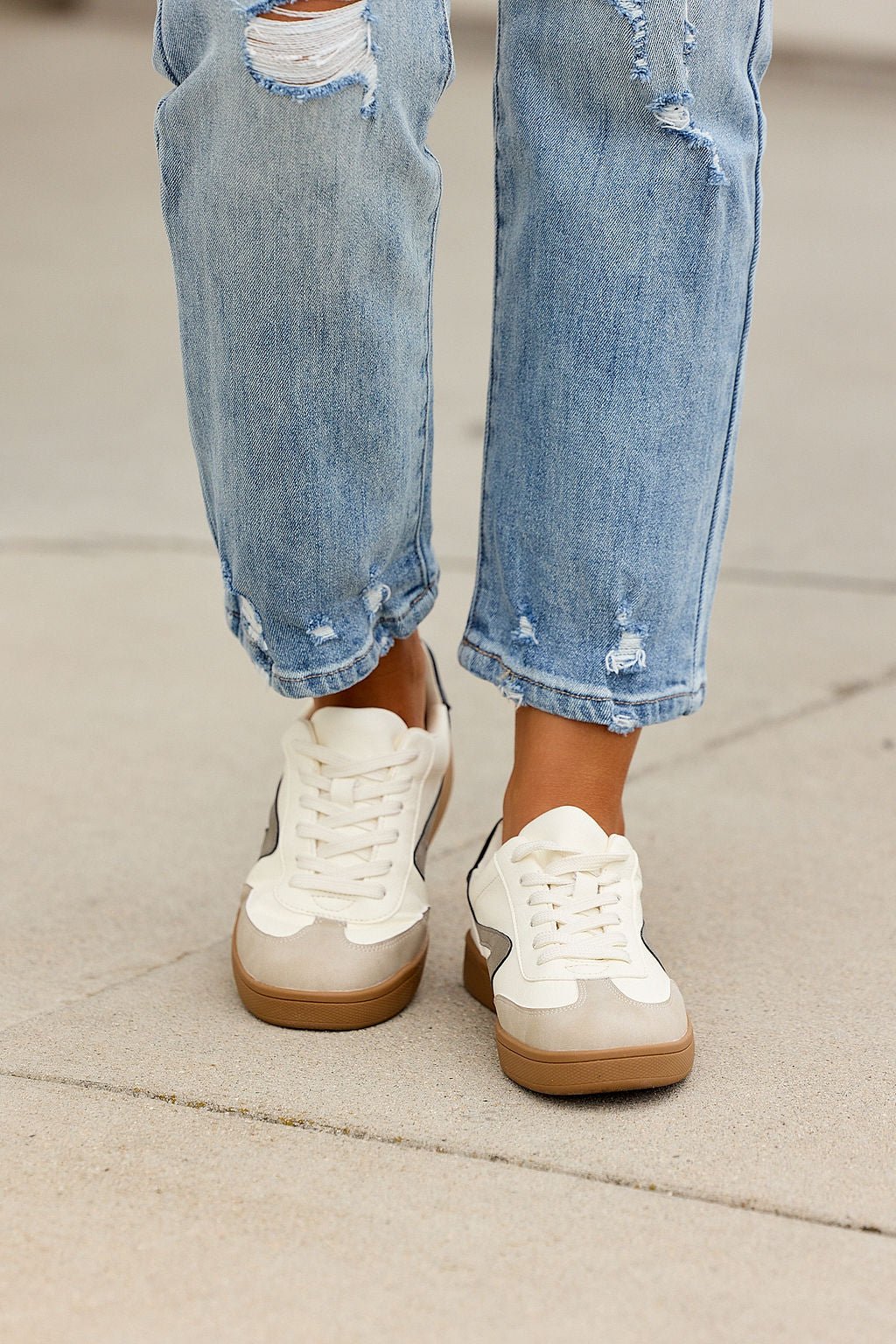 Person in light-wash ripped jeans and Dolce Vita Voyage Sneakers - Grey, standing on concrete.