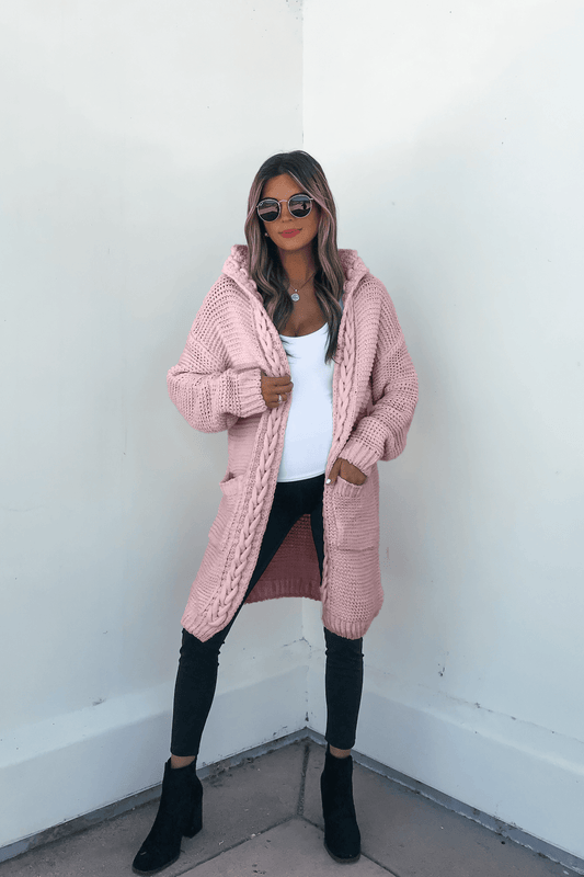 Woman wearing sunglasses, a white top, black pants, and the Dusty Rose Braided Trim Hooded Cardigan against a white wall.