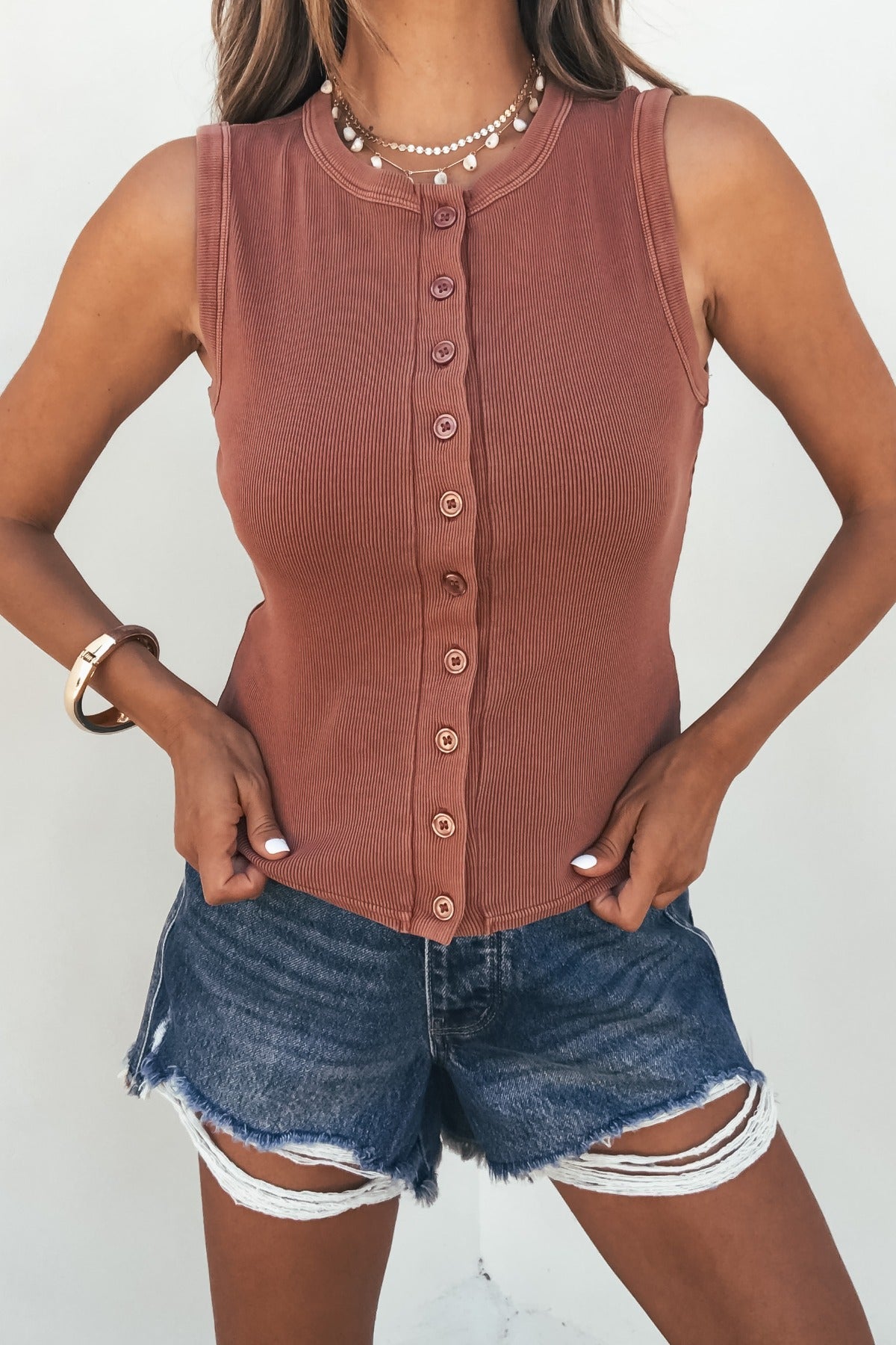 Woman wears the Easy Days Button Front Tank Top in terracotta with distressed denim shorts, styled with necklaces and a bracelet.