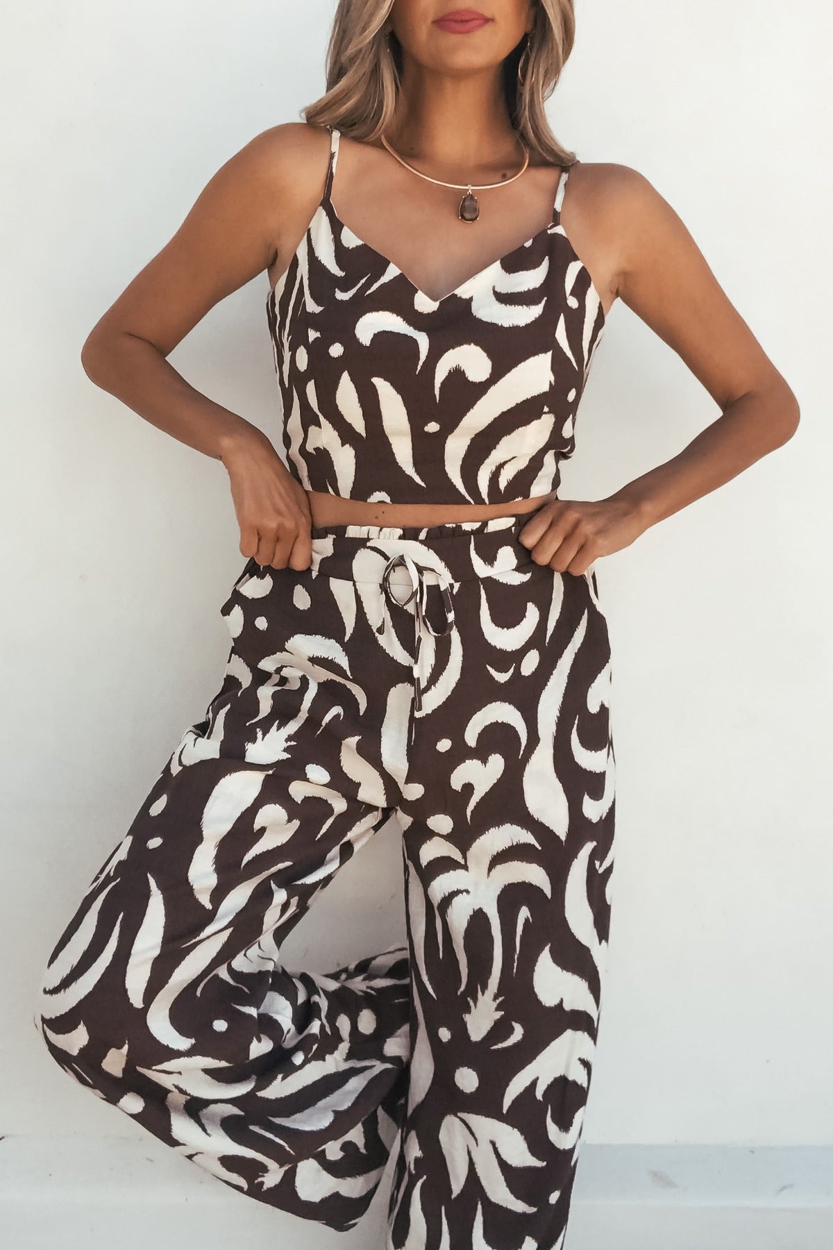 Woman wears the Eda Print Cami Tank and Pants Set in brown, featuring adjustable straps, against a plain white background.