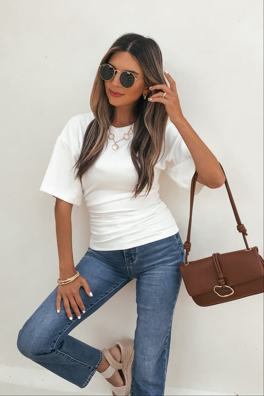 Woman in sunglasses, blue jeans, beige shoes, and a brown bag wears the Effortless Everyday Ruched Top - White against a white wall.