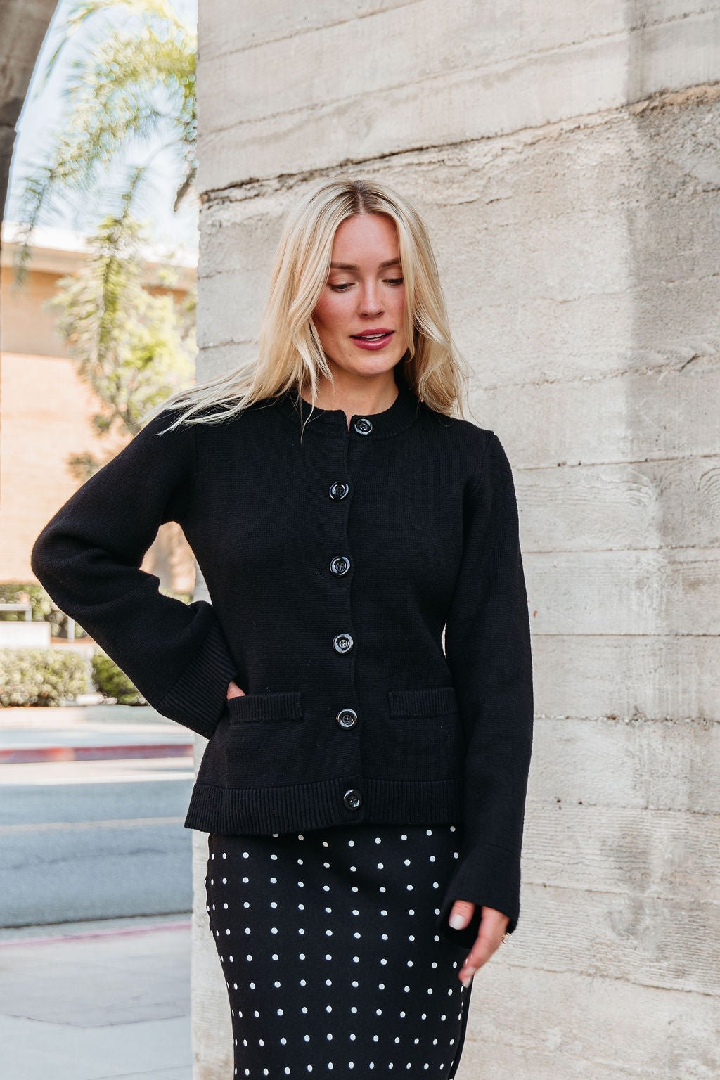 A woman in an Elan Black Button Up Cardigan Jacket stands near a concrete wall outdoors.