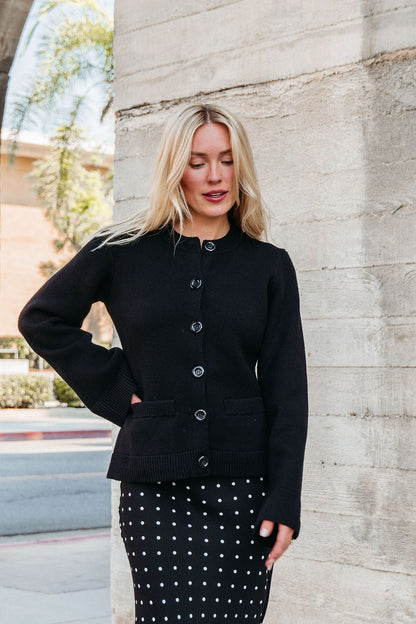 A woman in an Elan Black Button Up Cardigan Jacket stands near a concrete wall outdoors.