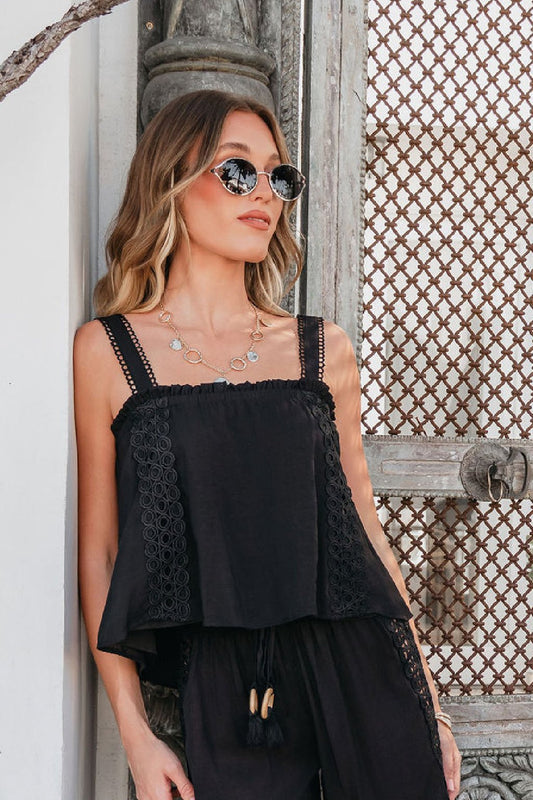 A woman stands confidently by a decorative door, wearing the ELAN Black Lace Trim Tank Top and stylish sunglasses.