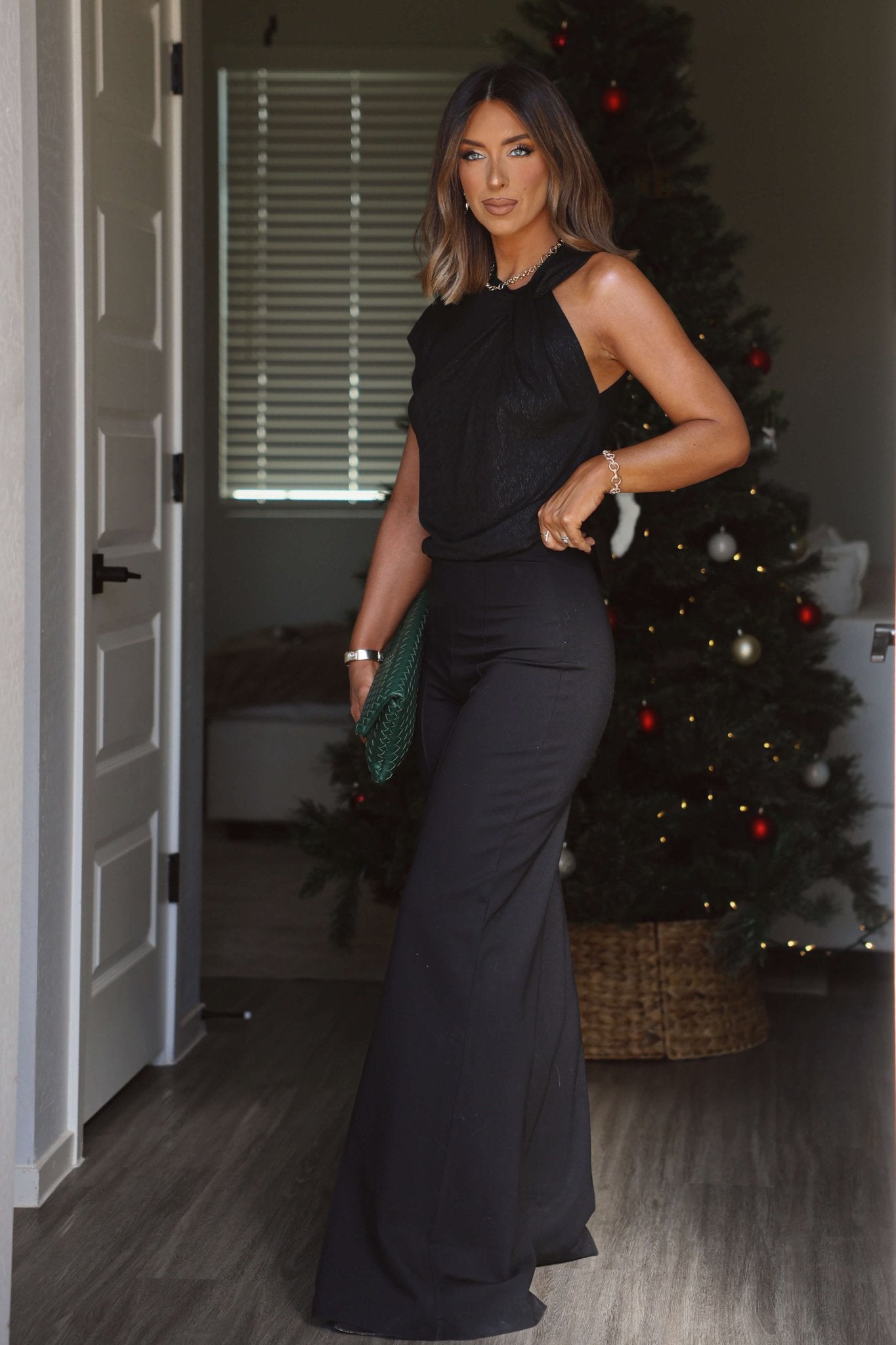 Woman in Elan Black Seam Detail Wide Leg Pull-On Pants stands by a Christmas tree, holding a green clutch.
