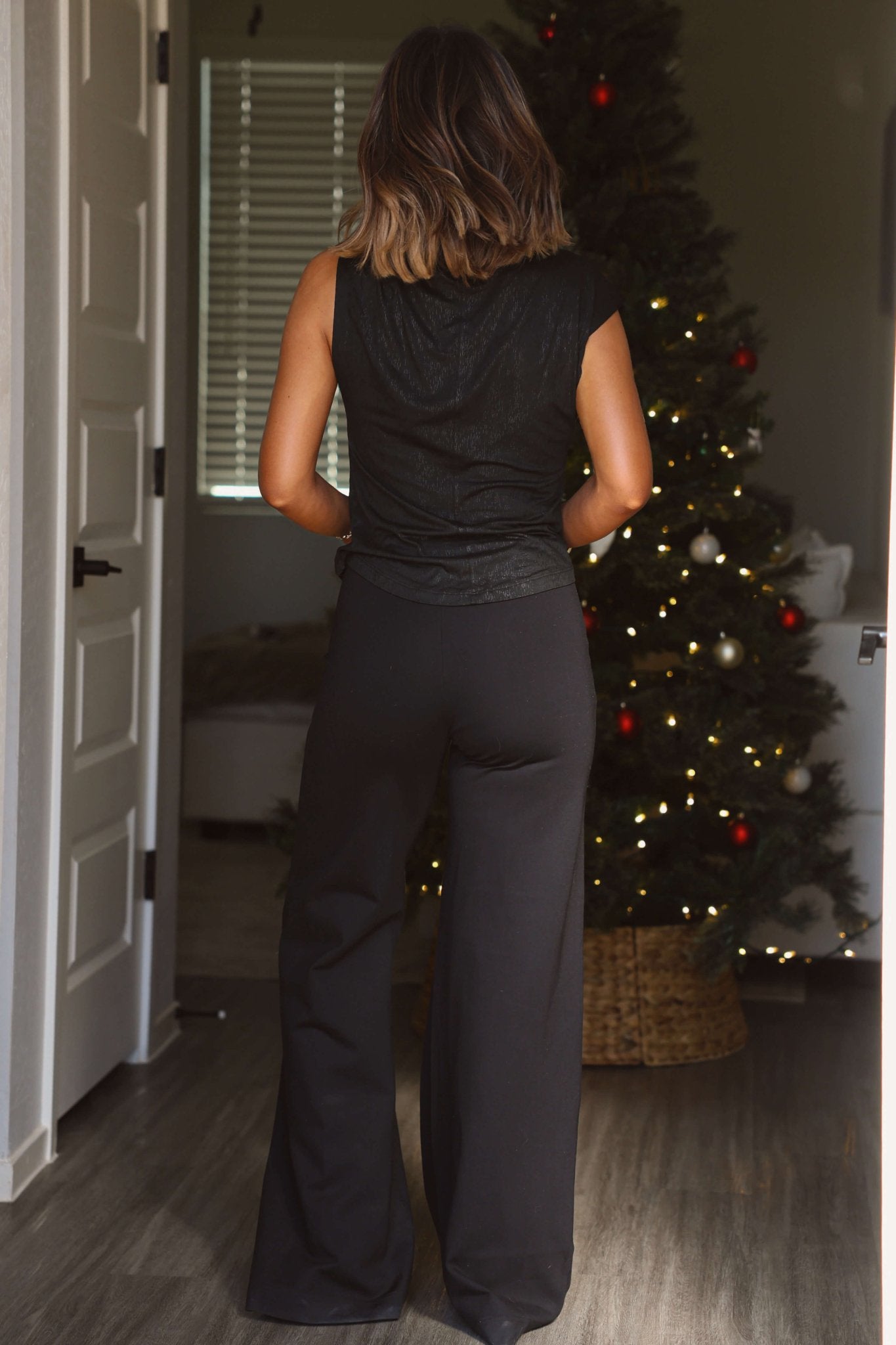 A woman stands indoors near a decorated Christmas tree, wearing Elan Black Seam Detail Wide Leg Pull-On Pants.