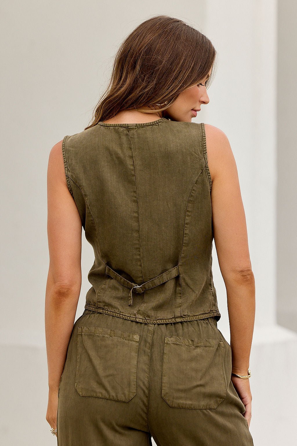 Woman wearing the ELAN Button Up Vest - Olive, sleeveless jumpsuit style, shown from the back against a light background.