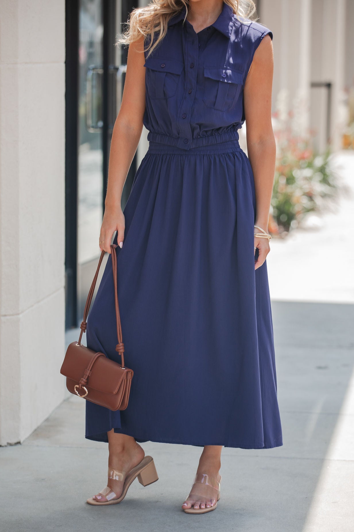 Woman wearing the Elan Collared Button Down Top in navy, clear heeled sandals, and a brown shoulder bag, standing outdoors.