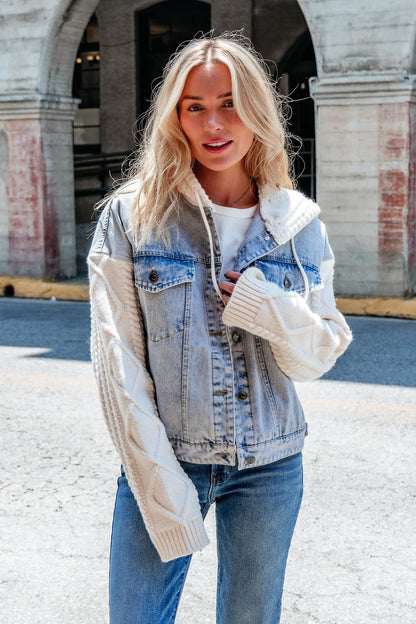 A woman wears the Elan Denim Hooded Sweater Jacket with cable knit sleeves, smiling outdoors on a city street.
