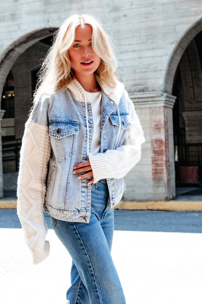 Blonde woman in Elan Denim Hooded Sweater Jacket with cable knit sleeves and blue jeans, standing outdoors in sunlight.