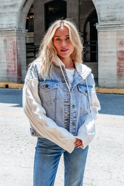 A woman with long blonde hair wears the Elan Denim Hooded Sweater Jacket over a white top and blue jeans on a sunny day.