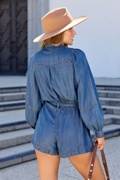 Woman wears the Elan Denim Long Sleeve Belted Romper, tan wide-brim hat, and holds a brown bag near outdoor stone steps.