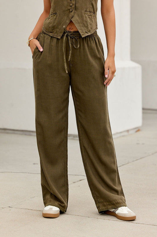 Person wearing ELAN Elastic Drawstring Pants in olive, paired with a matching sleeveless top, standing on a sidewalk hands in pockets.