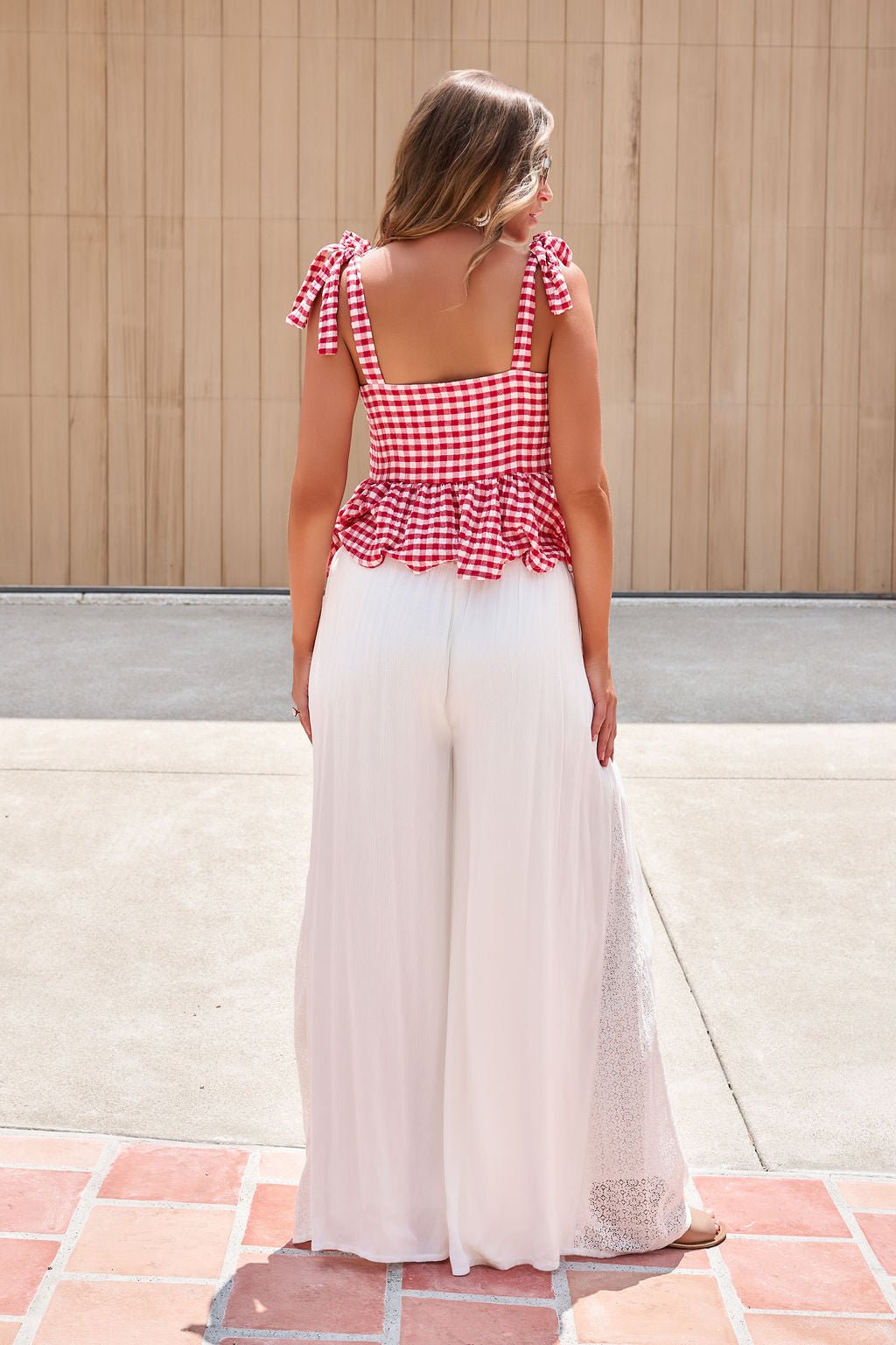 A woman stands outside in a red gingham tie-strap top and Elan Flowy Wide Leg Pants - Ivory with an elastic waistband.