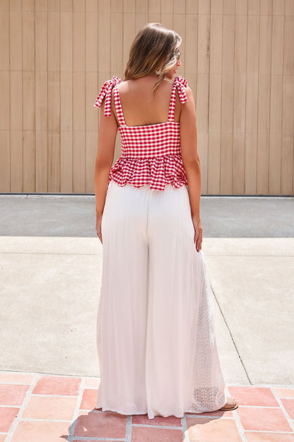 A woman stands outside in a red gingham tie-strap top and Elan Flowy Wide Leg Pants - Ivory with an elastic waistband.