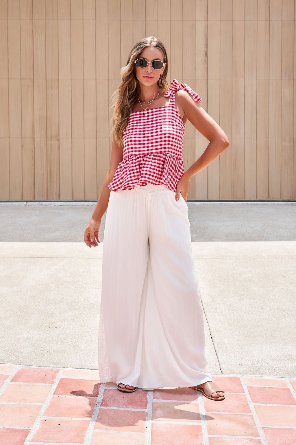 Woman in a red checkered sleeveless top and Elan Flowy Wide Leg Pants - Ivory, standing outdoors on a sunny day.
