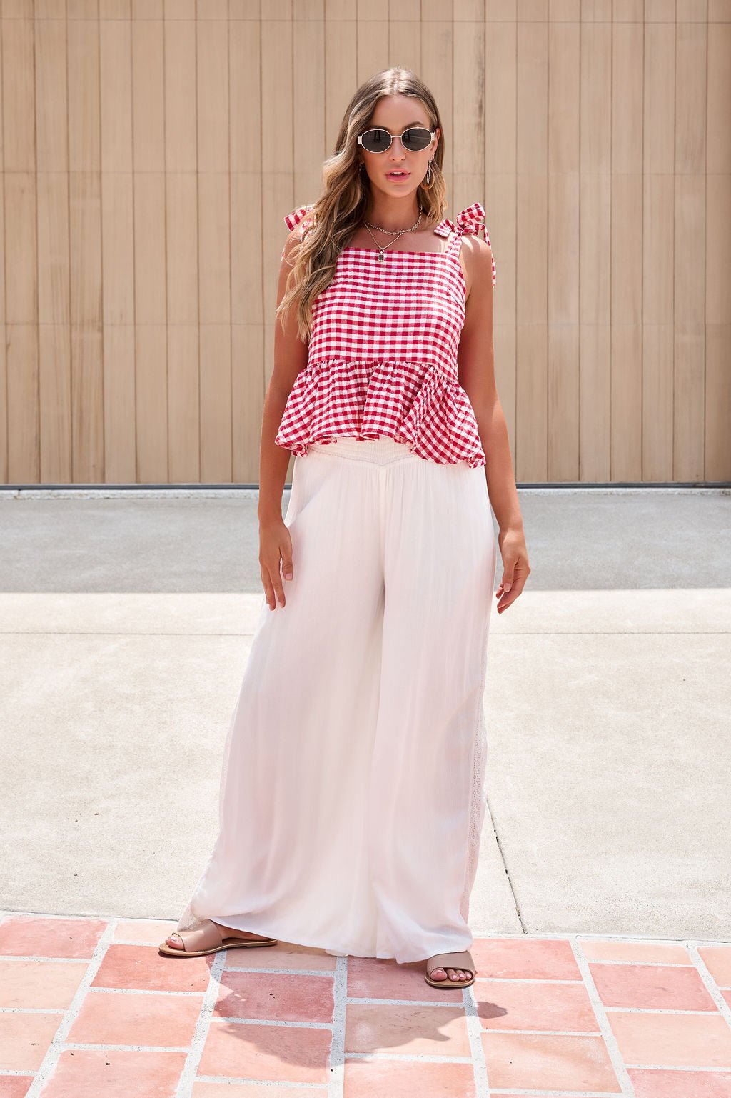 Woman wearing a red gingham top, Elan Flowy Wide Leg Pants - Ivory, and sandals stands on a tiled patio.