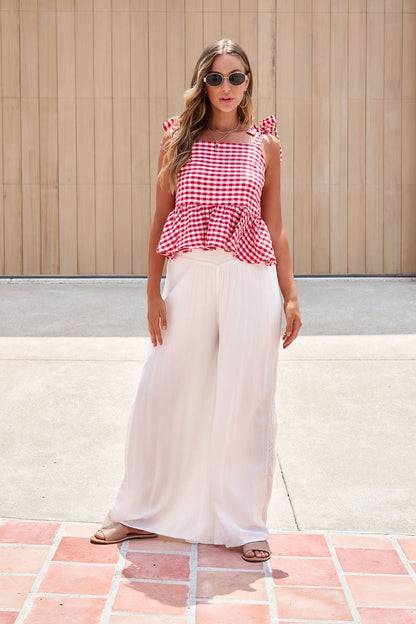Woman wearing a red gingham top, Elan Flowy Wide Leg Pants - Ivory, and sandals stands on a tiled patio.