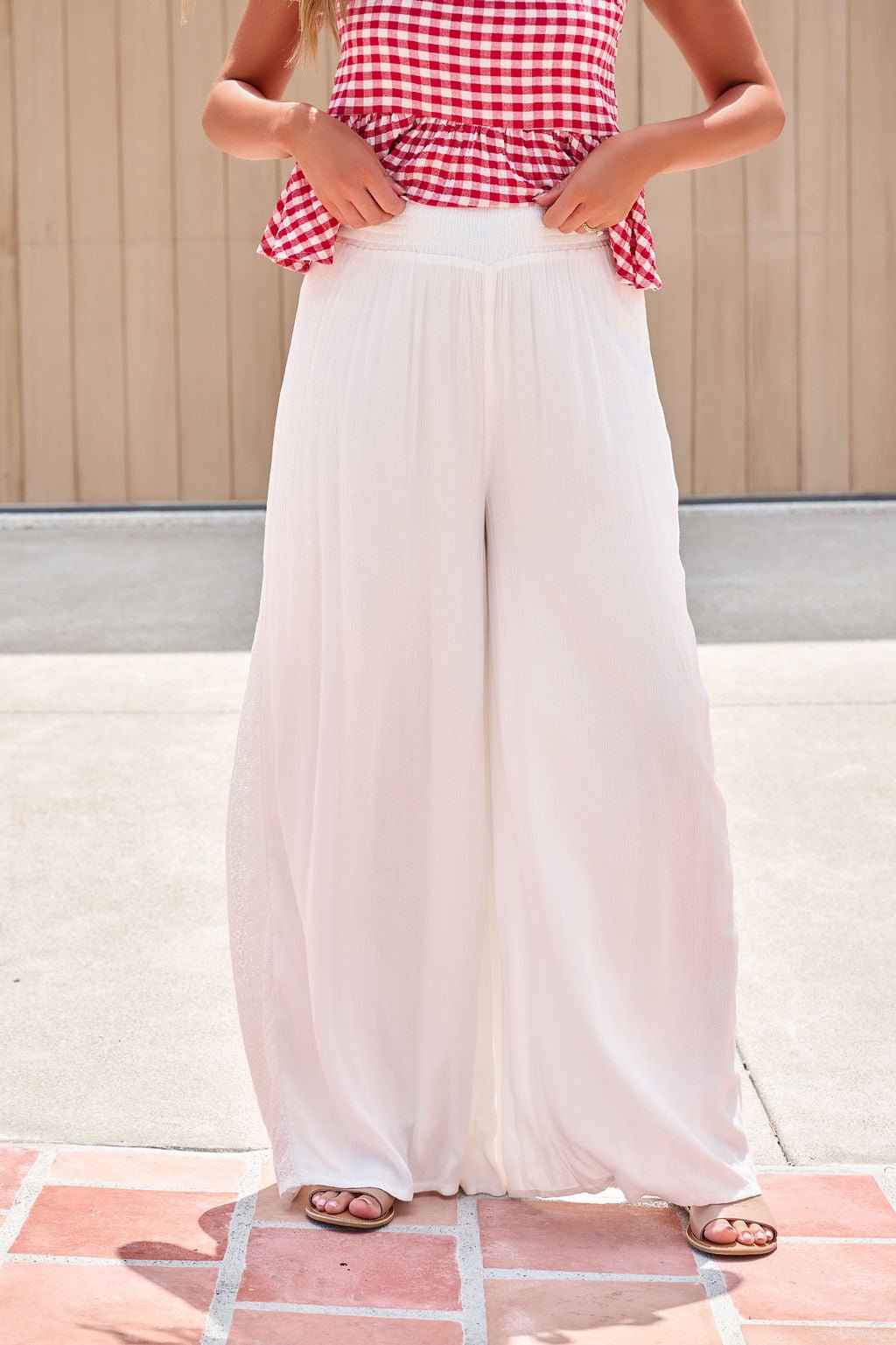Person in a red gingham sleeveless top and Elan Flowy Wide Leg Pants - Ivory, standing outdoors on a tiled surface.