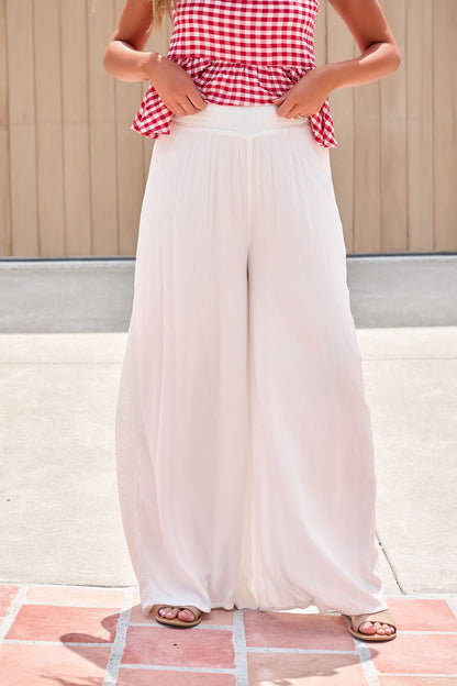 Person in a red gingham sleeveless top and Elan Flowy Wide Leg Pants - Ivory, standing outdoors on a tiled surface.