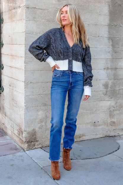 Woman stands outside in the Elan Grey and White Cable Knit Sweater, paired with blue jeans and brown suede ankle boots.