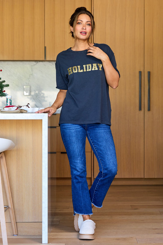 Woman wears the Elan Grey Holiday Graphic Tee, blue jeans, and slippers in a modern kitchen with festive holiday decor.