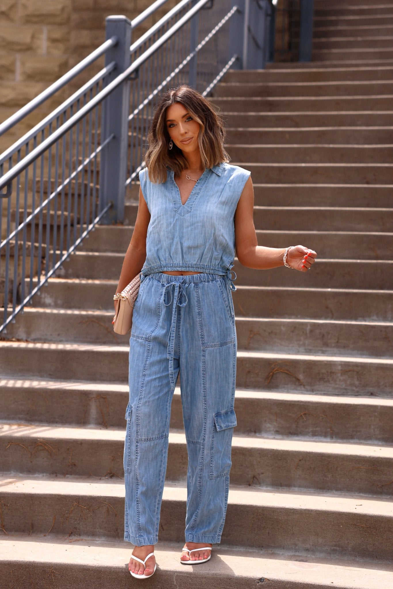 Woman on outdoor steps in Elan Jetset Denim Cargo Pants, holding a clutch and wearing sandals.