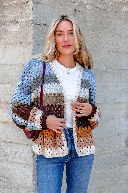 A woman wears the Elan Multi Striped Crochet Open Cardigan and blue jeans, holding a purple bag, facing the camera.