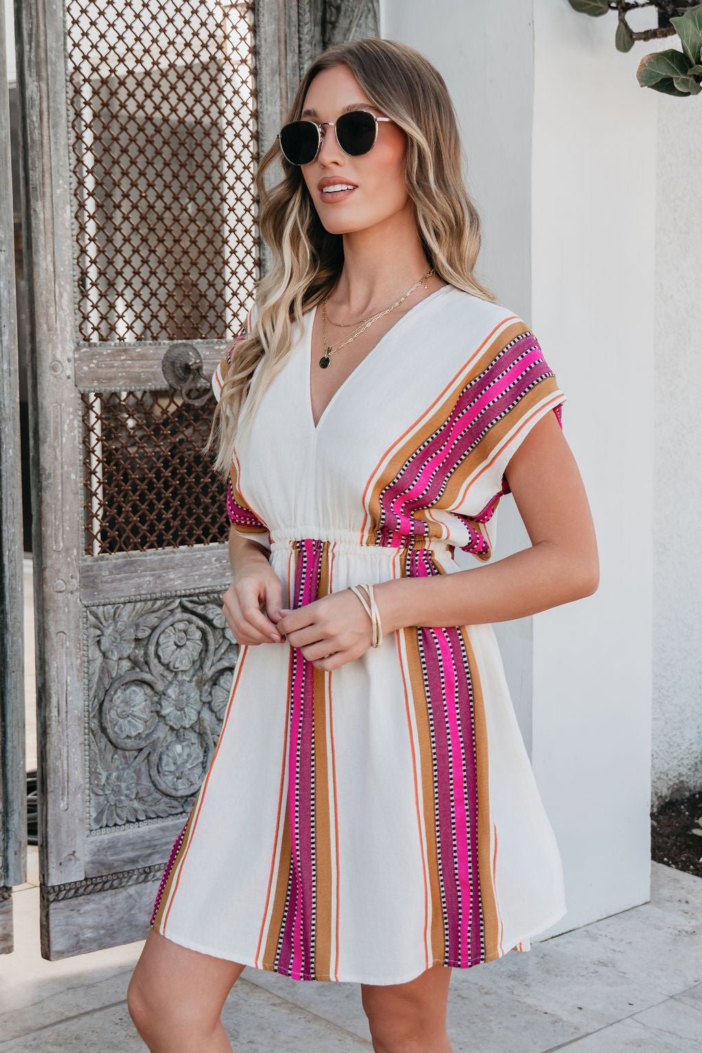 Woman in the ELAN Natural Striped Kimono Dress with an elastic waist and sunglasses—ideal resort wear by a decorative door.