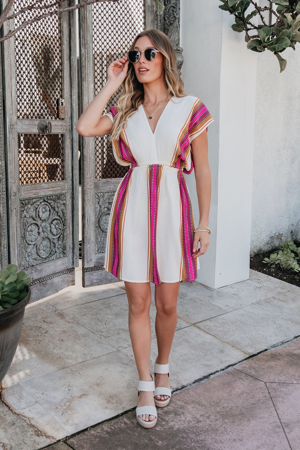 Woman in the ELAN Natural Striped Kimono Dress with sunglasses—perfect resort wear by a metal gate and potted plant.