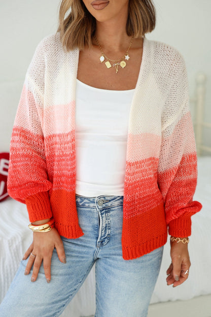 A woman wearing an Elan Red Ombre Open Front Cardigan, white top, blue jeans, and gold jewelry indoors.