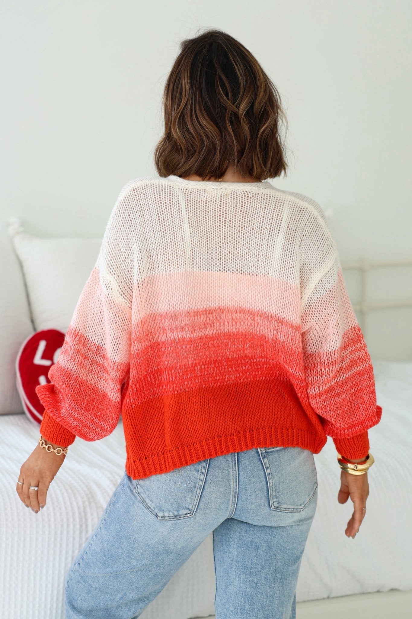 A person with wavy brown hair wears an Elan Red Ombre Open Front Cardigan and light blue jeans, facing away from the camera.