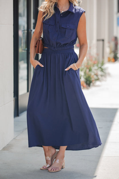 Woman in a sleeveless navy top and Elan Smocked Midi Skirt - Navy, holding a small brown purse on the sidewalk.