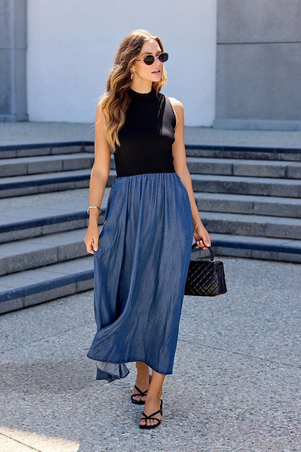 Woman in sunglasses wears the Elan Two Tone Midi Dress - Navy and carries a black bag while walking outdoors.